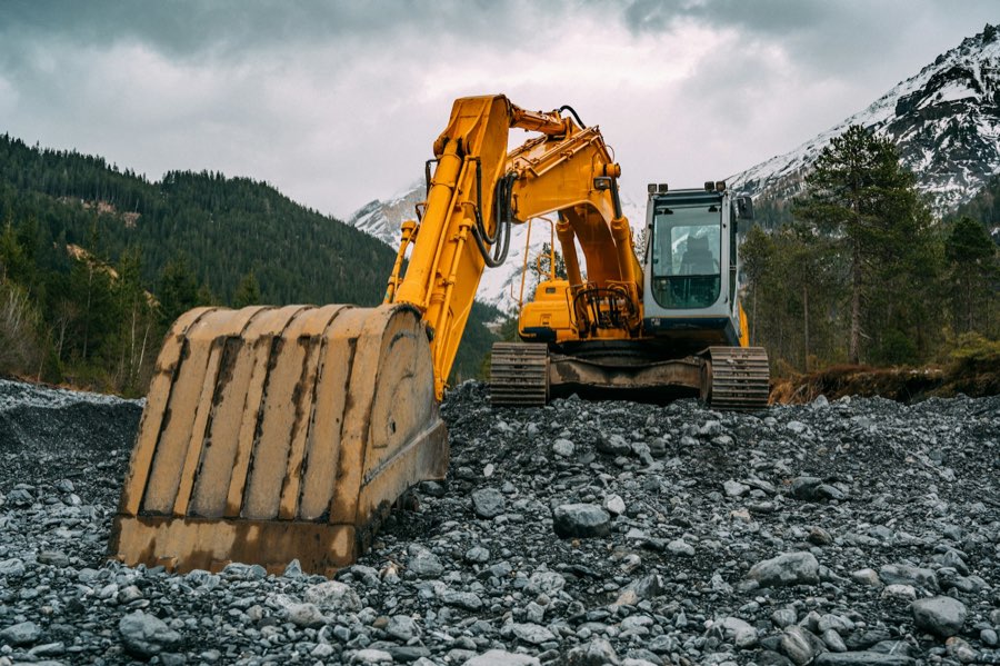 Excavator working a rocky site below forested New England hills